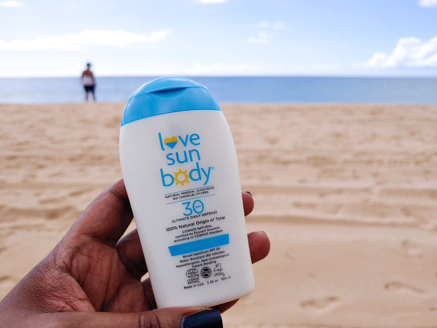 patranila holds a bottle of love sun body sunscreen at the beach