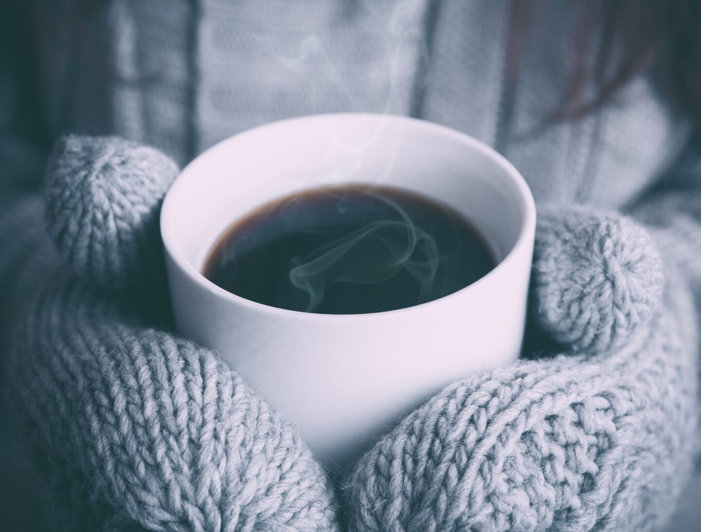 gloved hands holding steaming hot coffee