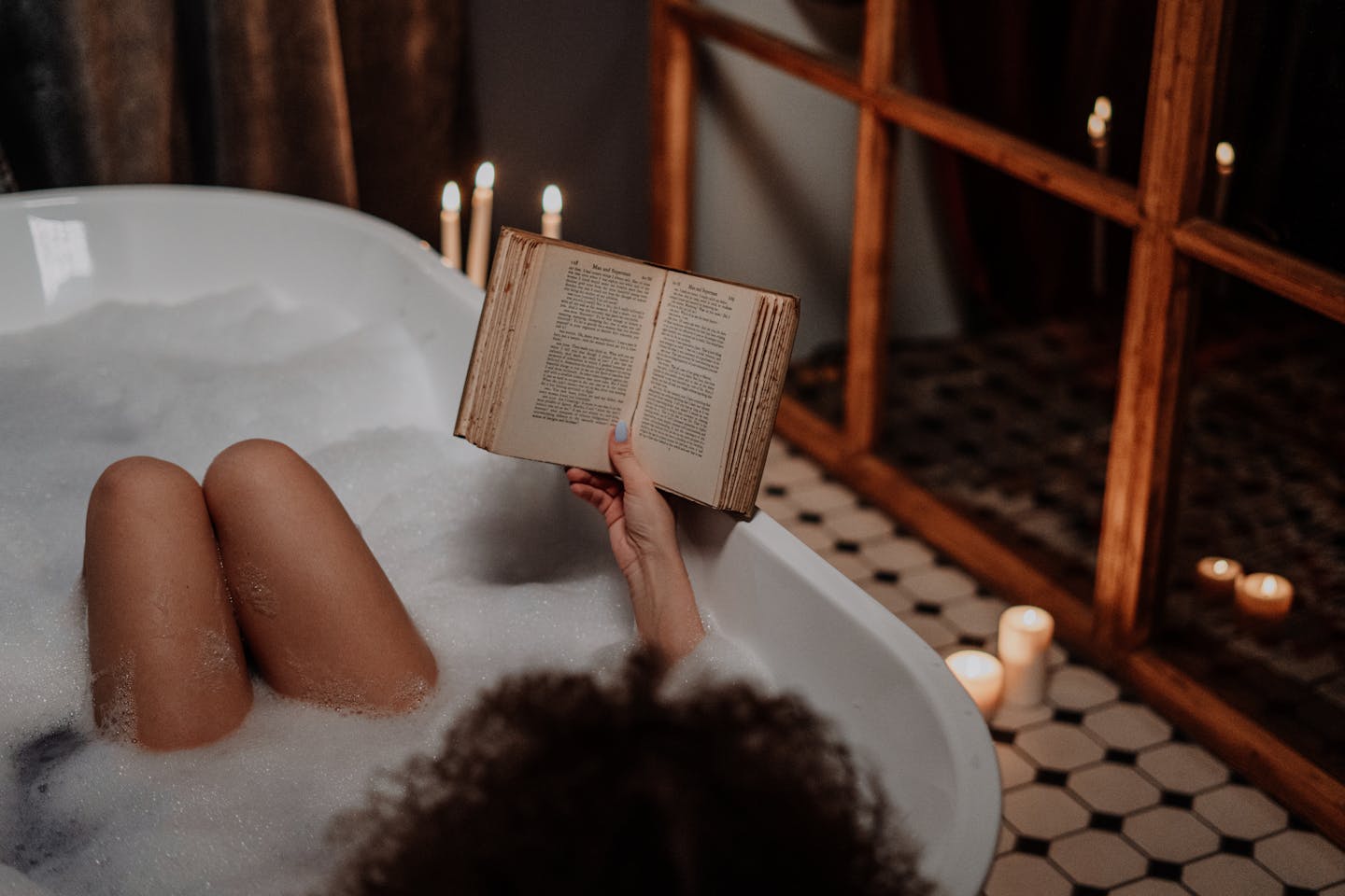 A peaceful scene of a woman enjoying a milky bubble bath while reading by candlelight.